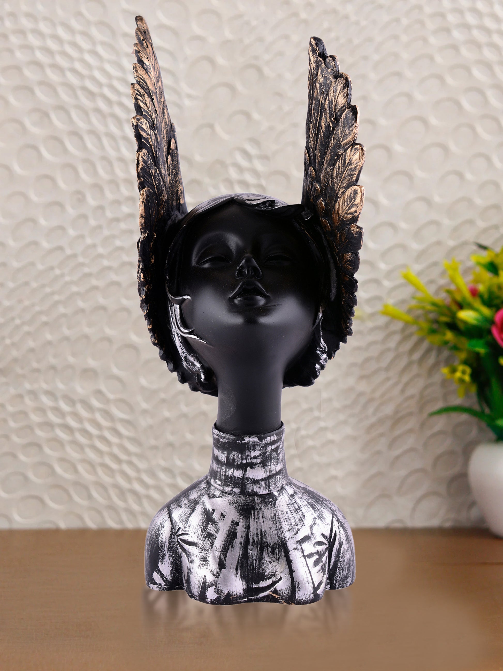 Black mannequin head with decorative wings on a textured wall background